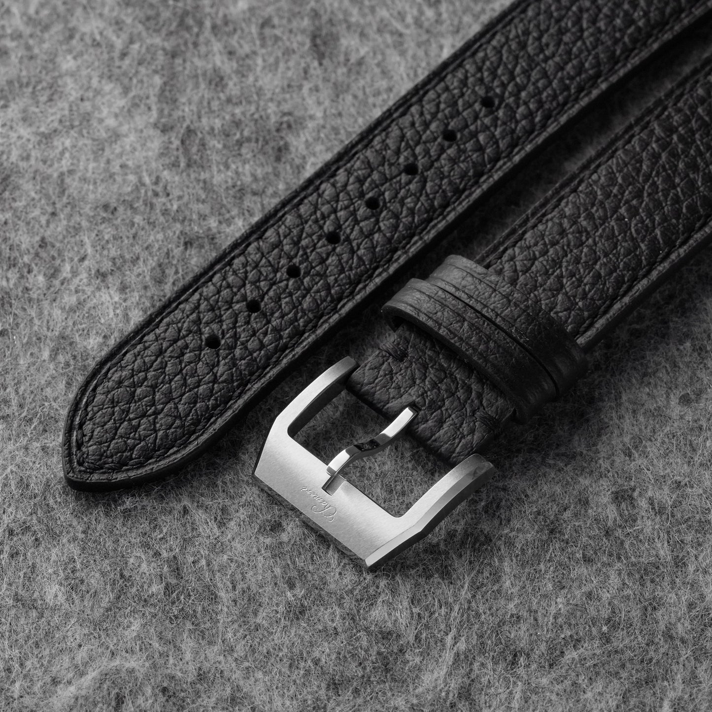 Close-up of black pebbled leather texture and silver-tone watch buckle