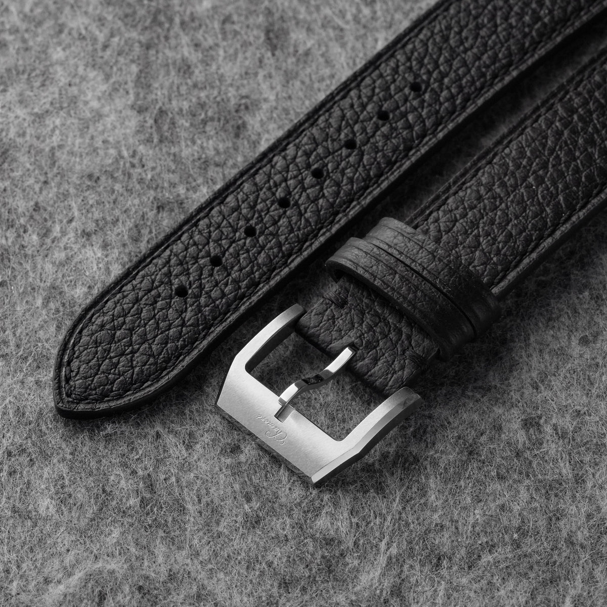 Close-up of black pebbled leather texture and silver-tone watch buckle