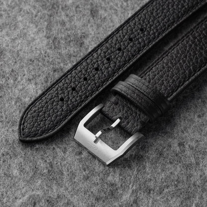 Close-up of black pebbled leather texture and silver-tone watch buckle